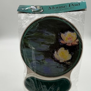 May include: A round mouse pad with a built-in wrist rest featuring a painting of water lilies by Claude Monet. The pad is white with a green border and the wrist rest is green. The text "Monet" is printed on the pad.