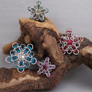 May include: Four silver star-shaped jewelry pieces with different colored gemstones in the center. The stars are on a piece of driftwood.