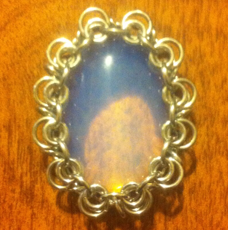 May include: A silver chainmail pendant featuring a large, iridescent opal cabochon in the centre.