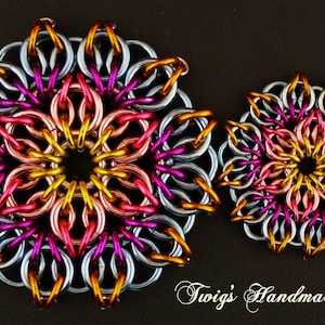 Puede incluir: Dos diseños florales de cota de malla hechos a mano en plata, oro, rosa y morado. La flor más grande tiene aproximadamente 7.6 cm de diámetro, y la más pequeña, unos 5 cm. El texto "Twig's Handmade" está en la esquina inferior derecha.