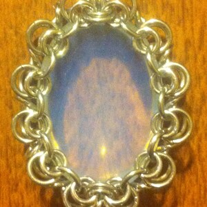 May include: A silver chainmail pendant with a round, iridescent opal-like stone in the centre.