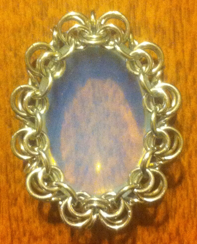 May include: A silver chainmail pendant with a round, iridescent opal-like stone in the centre.