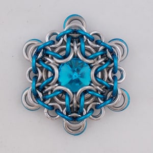 May include: A silver and blue metal snowflake with a turquoise gemstone in the center.
