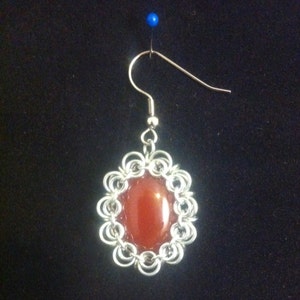 May include: A silver chainmail earring with a red carnelian stone.