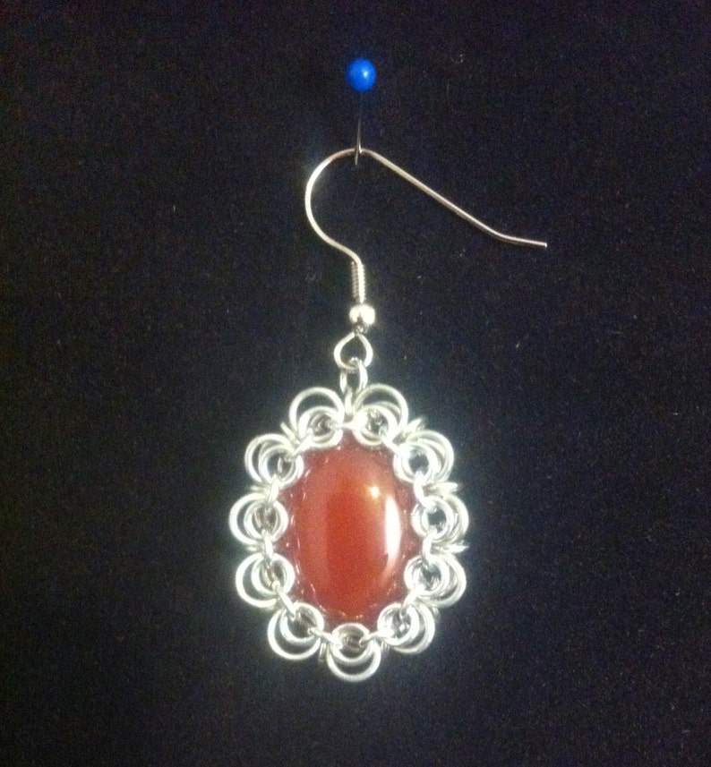 May include: A silver chainmail earring with a red carnelian stone.