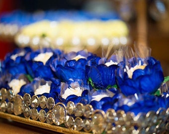 May include: A tray of blue and white flower-shaped candies, arranged in rows on a gold tray with a crystal-like border.