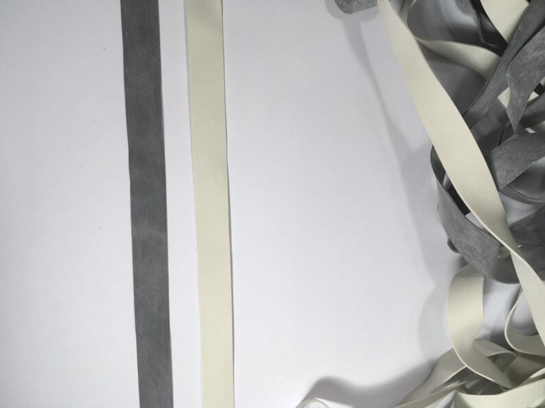 May include: Two strips of elastic, one white and one gray, are laid out on a white surface. A pile of the same white elastic is in the lower right corner of the image.