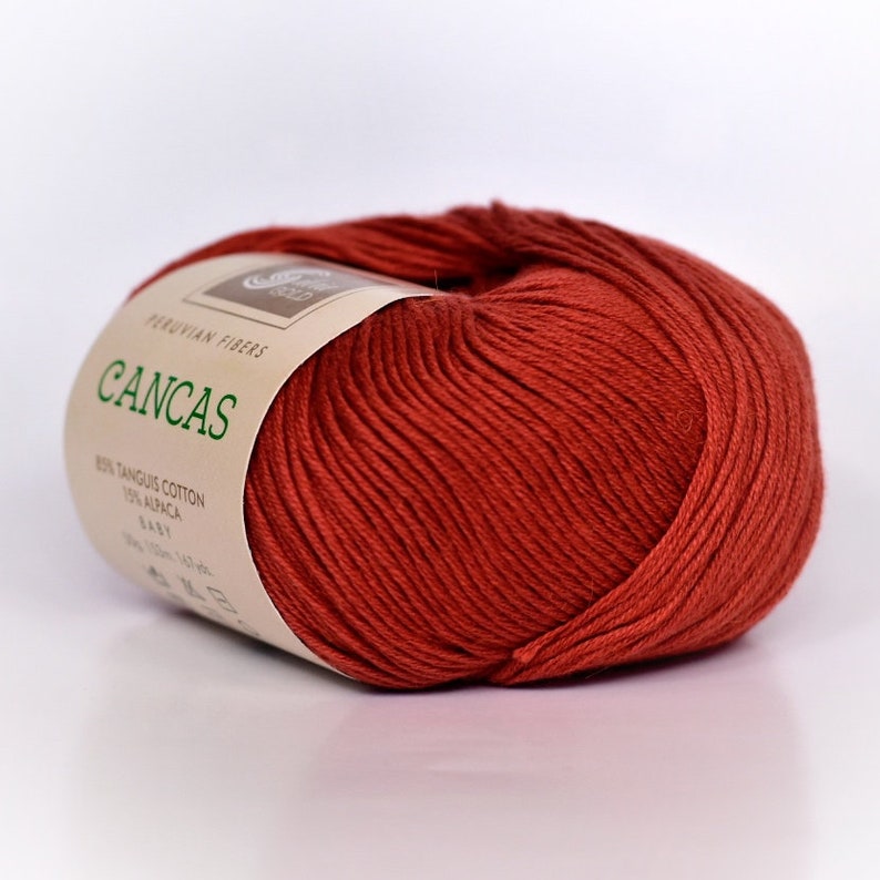 May include: A ball of red yarn labeled "Cancas" with the text "Peruvian Fibers 80% Tanguis Cotton 20% Alpaca Baby 100g - 140m - 142 yds" on the label.