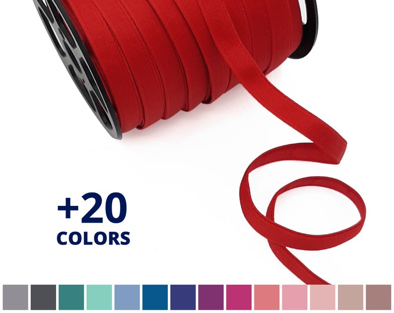 May include: A spool of red elastic trim with a +20 COLORS label. The trim is folded and wound around the spool. A length of the trim is hanging off the spool, showing the texture and color of the trim.