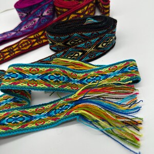 May include: Five colorful woven fabric ribbon trims with geometric patterns. The trims are in shades of red, black, blue, green, yellow, and purple. The trim on the bottom has a fringe.