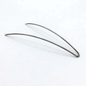 May include: A silver metal hair clip with rounded ends. The clip is bent into a curved shape.