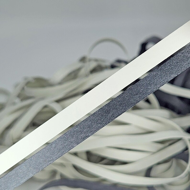 May include: Two strands of elastic cord, one white and one black, are shown against a white background. The cords are lying on top of a pile of other white elastic cords.