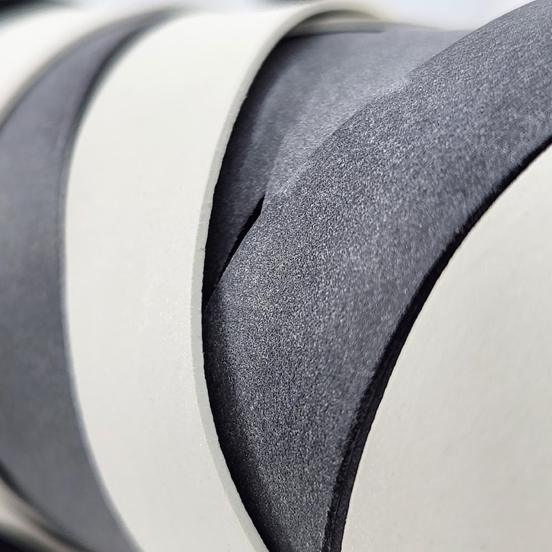 May include: Close-up of a white and gray fabric with a textured surface. The fabric is folded and layered, creating a pattern of overlapping curves.