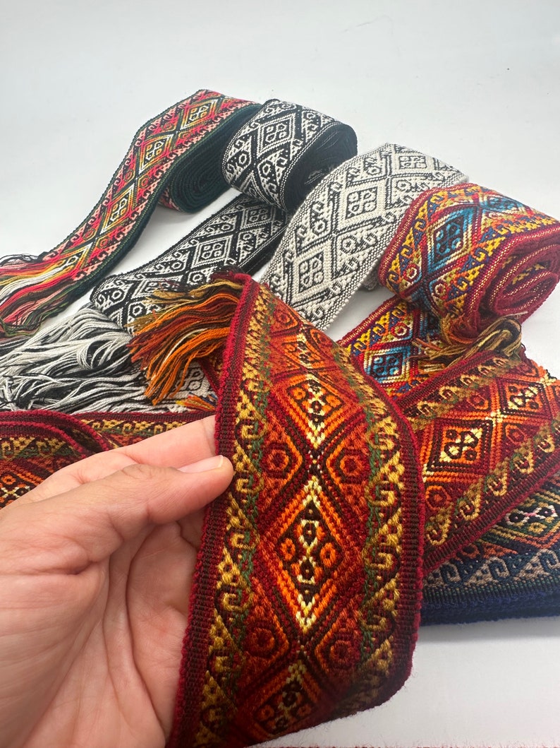 May include: Assortment of colourful woven ribbon trim with geometric patterns. The ribbon is red, orange, yellow, green, blue and black. The ribbon is rolled up and has a fringe on the ends.