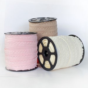 May include: Three spools of lace trim, one pink, one beige, and one white. The spools are on a white surface.