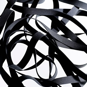 May include: A close-up of a tangled pile of black elastic ribbon. The ribbon is woven and has a textured surface.