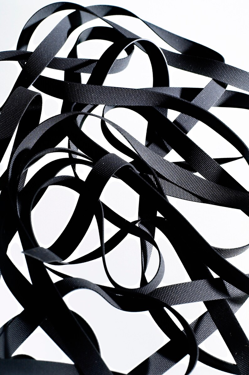 May include: A close-up of a tangled pile of black elastic ribbon. The ribbon is woven and has a textured surface.