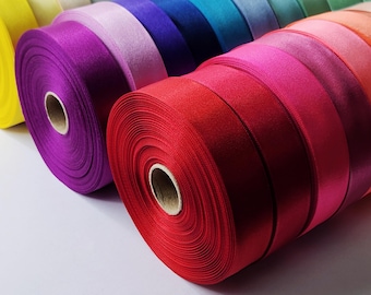 May include: A collection of colorful satin ribbon spools in various shades of yellow, pink, purple, blue, green, red, and orange. The spools are arranged in a row, with the red spool in the foreground.