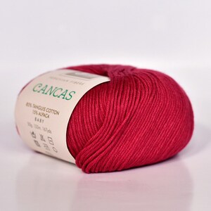 May include: A ball of red yarn labeled "CANCAS" with the text "85% Tangus Cotton 15% Alpaca Baby 50g 153m 167yds".