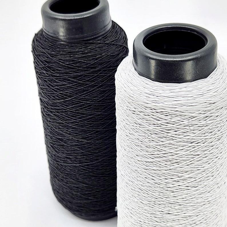 May include: Two spools of elastic thread, one black and one white. The spools are made of plastic and have a black top.