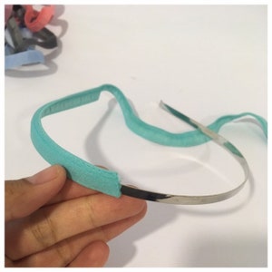 May include: A turquoise headband with a silver metal band. The headband is made of fabric and is soft and comfortable to wear.