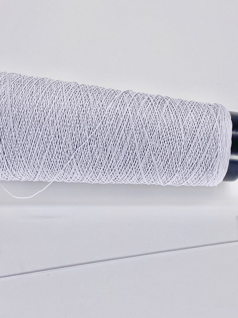 May include: A spool of white elastic thread wound around a black plastic bobbin.