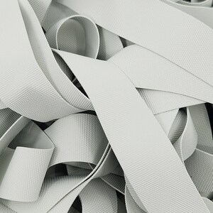 May include: A close-up of a pile of white elastic ribbon. The ribbon is woven with a textured pattern.