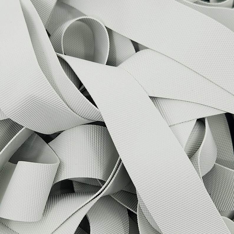 May include: A close-up of a pile of white elastic ribbon. The ribbon is woven with a textured pattern.