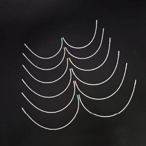 May include: A selection of white, curved plastic components, each with a gentle arc. Some have small coloured sections, including blue, yellow, and pink, at the centre. The background is a solid black.