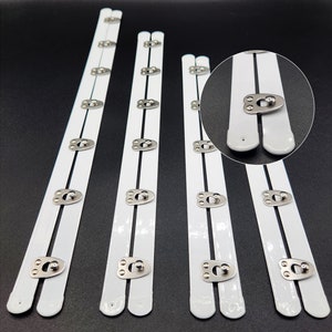 May include: Five white bra strap extenders with silver metal hooks and eyes. The extenders are different lengths, with the shortest being about 6 inches long and the longest being about 10 inches long.