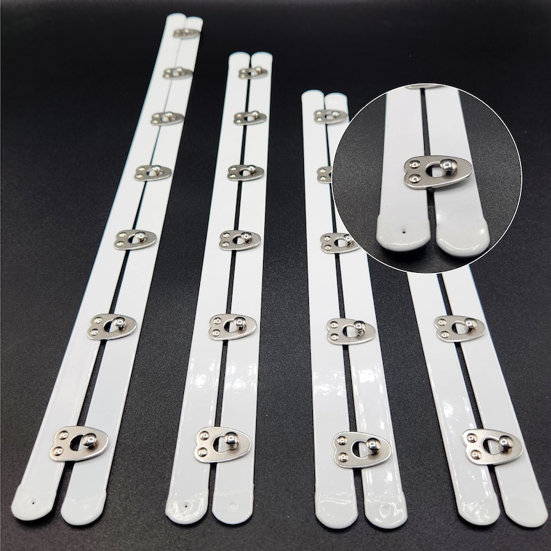 May include: Five white bra strap extenders with silver metal hooks and eyes. The extenders are different lengths, with the shortest being about 6 inches long and the longest being about 10 inches long.