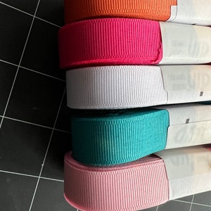 May include: Five spools of ribbon in different colors. The colors are orange, pink, white, teal, and light pink.