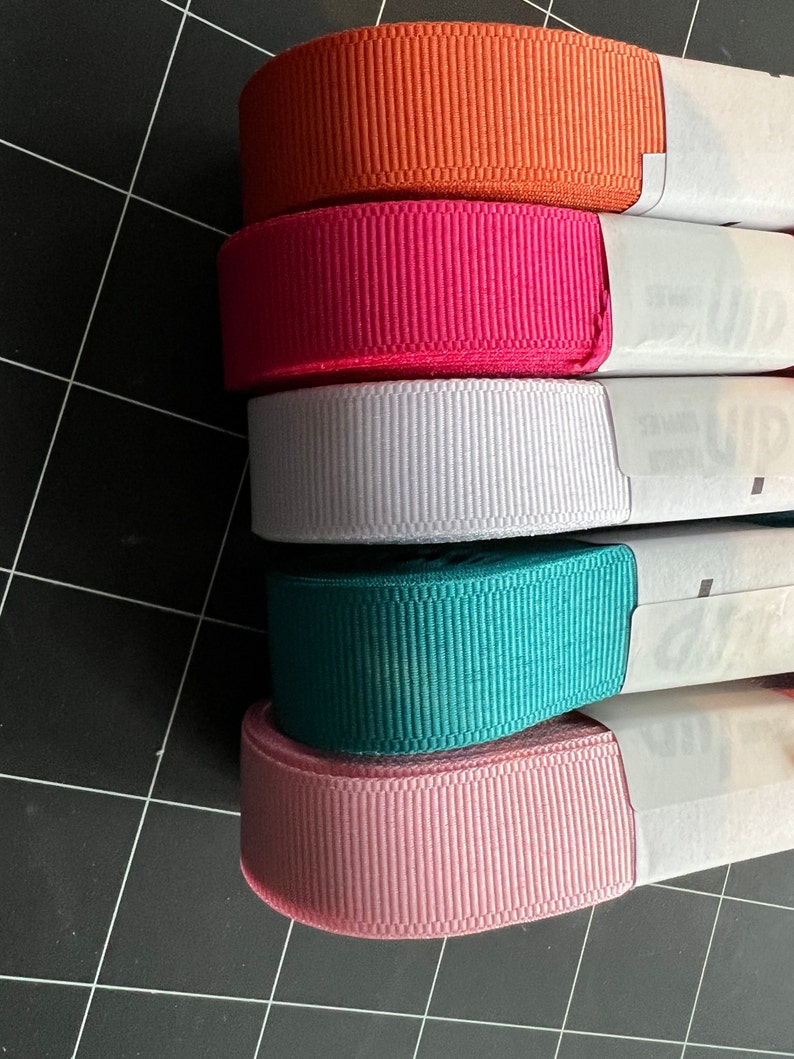May include: Five spools of ribbon in different colors. The colors are orange, pink, white, teal, and light pink.