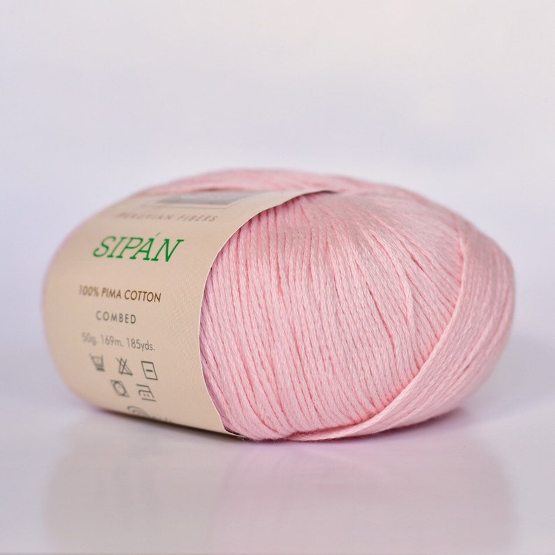 May include: A pink ball of yarn labeled "SIPAN 100% PIMA COTTON COMBED 50g 169m. 185yds."
