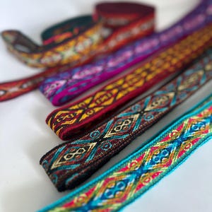 May include: Assortment of colorful woven ribbon trim with geometric patterns. The ribbon is made of a soft, textured fabric and features a variety of colors, including red, blue, yellow, green, and black.