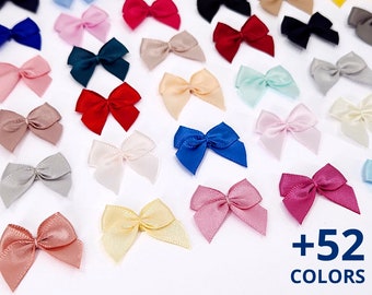 May include: A collection of over 52 colors of small satin ribbon bows. The bows are arranged in rows on a white surface. The colors include red, blue, green, yellow, pink, purple, and many more.