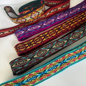 May include: Assortment of colourful woven ribbon trim with geometric patterns. The ribbon is in shades of red, orange, yellow, green, blue, purple, and black.