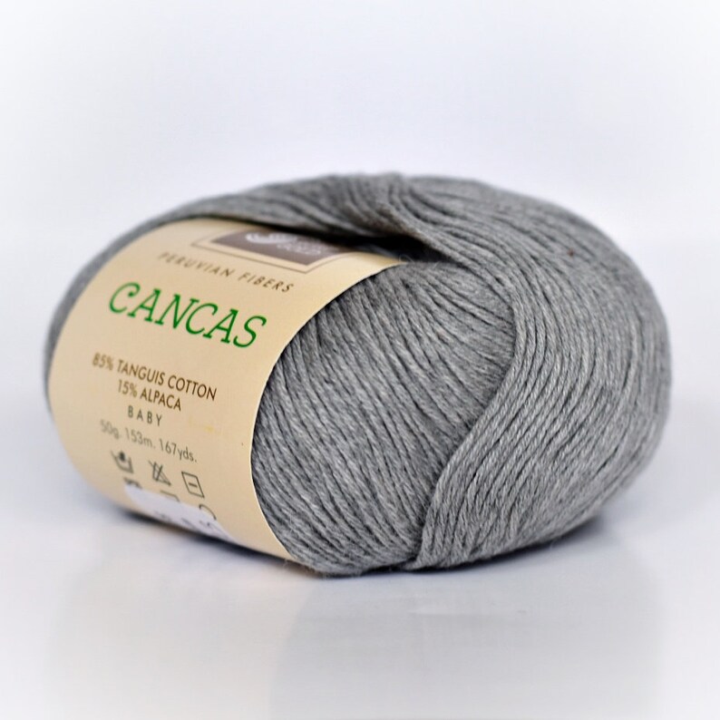 May include: A skein of gray yarn labeled "CANCAS" with the text "PERUVIAN FIBERS 85% TANGUIS COTTON 15% ALPACA BABY 50g 153m. 167yds."