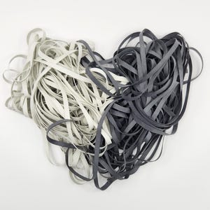 May include: Two spools of elastic cord, one white and one black, are tangled together. The cords are about 1/4 inch wide.