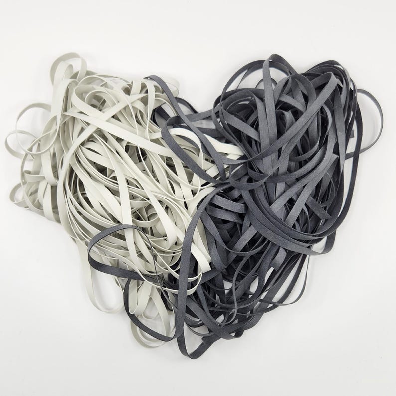 May include: Two spools of elastic cord, one white and one black, are tangled together. The cords are about 1/4 inch wide.