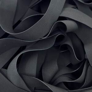 May include: A close-up of a pile of black elastic webbing. The webbing is woven with a textured pattern.