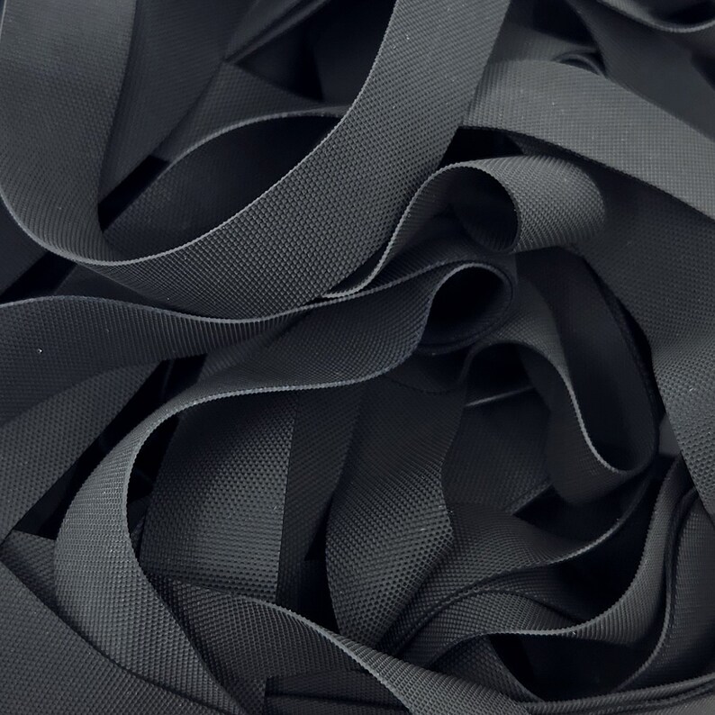 May include: A close-up of a pile of black elastic webbing. The webbing is woven with a textured pattern.
