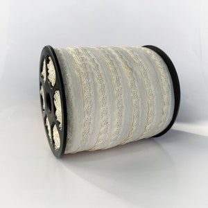 May include: A spool of white elastic trim with a silver glitter design. The trim is wound around a black plastic spool.