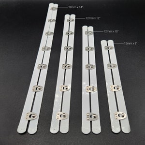 May include: Four white bra strap extenders with silver metal hooks and eyes. The extenders are 14 inches, 12 inches, 10 inches, and 8 inches long.