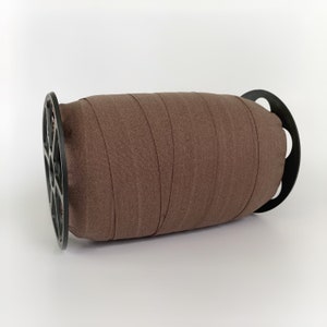 Peut inclure: Une bobine de ruban &eacute;lastique brun enroul&eacute; autour d'une bobine en plastique noir.