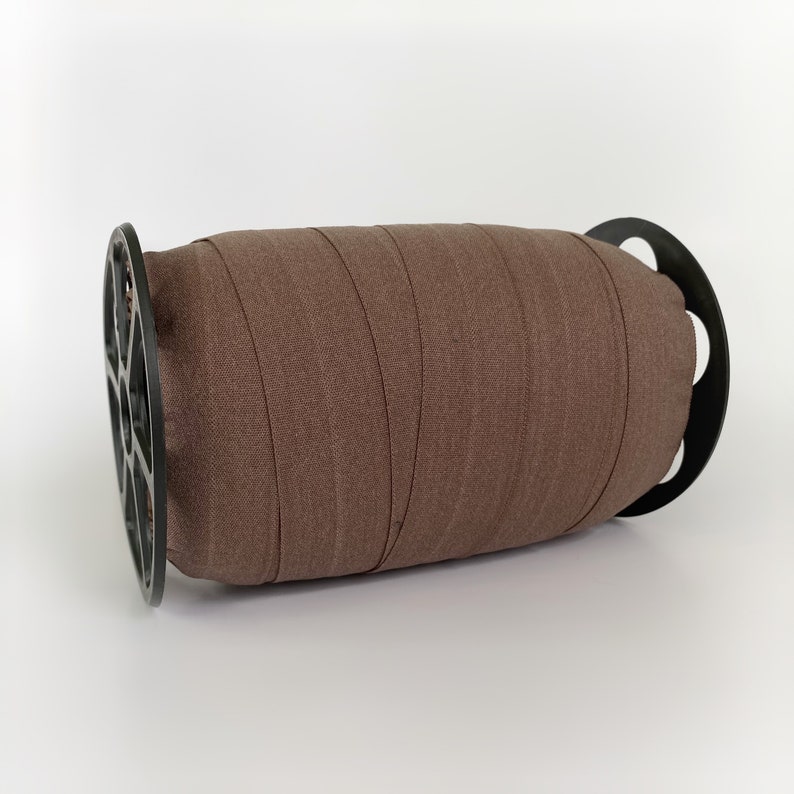 Peut inclure: Une bobine de ruban &eacute;lastique brun enroul&eacute; autour d'une bobine en plastique noir.