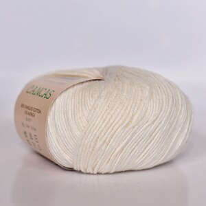 May include: A ball of white cotton yarn with a label that reads "CANCAS 100%  ANGORA COTTON  BRILLIANCA EASY 50g 130m"
