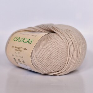 May include: A skein of beige yarn labeled "CANCAS" with the text "PERUVIAN FIBERS 85% TANGUIS COTTON 15% ALPACA BABY 50g. 153m. 167yds."
