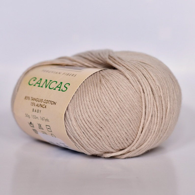 May include: A skein of beige yarn labeled "CANCAS" with the text "PERUVIAN FIBERS 85% TANGUIS COTTON 15% ALPACA BABY 50g. 153m. 167yds."