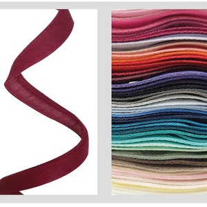 May include: A close-up of a burgundy satin ribbon, curled and twisted. The ribbon is shown against a white background. A stack of various colored ribbons is shown in the background.